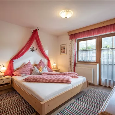 A cozy bedroom with a large bed and red decorative pillows. Soft lighting and a window create an inviting atmosphere.