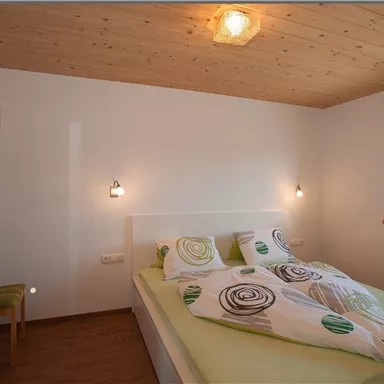 A cozy bedroom with a large bed and colorful blankets. The walls are bright, and there is a window that lets in a lot of light.