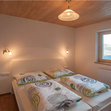 A modern bedroom with a large window and wooden ceiling. Two beds are decorated with colorful bedcovers.