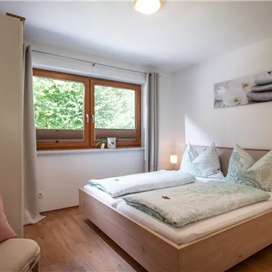 A modern bedroom with two beds, decorated in soft colors.  
Large windows let in plenty of daylight and offer a view of nature.