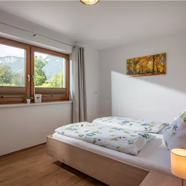 A cozy bedroom with a double bed and large windows. The room offers a view of a green landscape and is bright and inviting.
