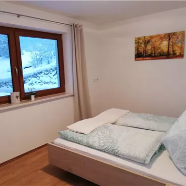 A cozy bedroom with a large window that looks out onto a snowy landscape. The comforter and pillows are in soft colors.