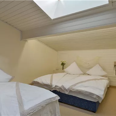 A cozy bedroom with two beds and bright bedding. The room has a lowered ceiling and a skylight that lets light in.