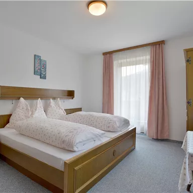 Ein einfaches Schlafzimmer mit zwei Einzelbetten und Holzverkleidung. Das Zimmer hat große Fenster und einen kleinen Tisch.