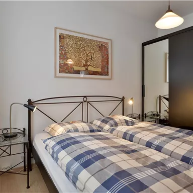 Ein gemütliches Schlafzimmer mit einem Doppelbett und karierten Bettdecken. An der Wand hängt ein Kunstwerk, und ein schwarzer Kleiderschrank steht neben dem Bett.