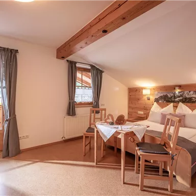 Ein gemütliches Zimmer mit einem Doppelbett und Holzdekor. Die Fenster bieten einen Blick nach draußen und es gibt einen Tisch mit Stühlen.