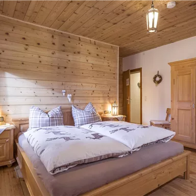 Ein gemütliches Schlafzimmer mit Holzdeko und warmem Licht. Das Zimmer ist mit einem Doppelbett und einem Holzschrank ausgestattet.