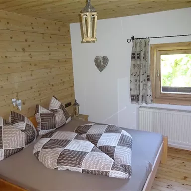 Ein gemütliches Schlafzimmer mit Holzverkleidung und einem großen Bett. Die Fenster lassen viel Tageslicht herein und schaffen eine einladende Atmosphäre.