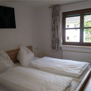 Ein gemütliches Schlafzimmer mit zwei Einzelbetten und weißen Bettdecken. Ein Fenster mit Blick ins Freie sorgt für natürliches Licht.