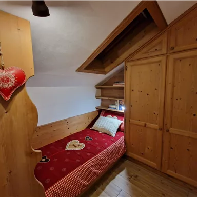 Ein gemütliches Schlafzimmer mit Holzmöbeln und einem roten Bett. An der Wand hängt ein herzförmiger Dekorationsgegenstand.