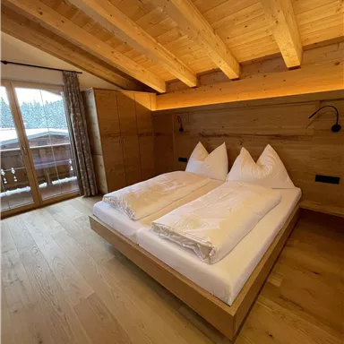 Ein gemütliches Schlafzimmer mit Holzwänden und einem großen Bett. Große Fenster bieten einen Blick nach draußen.