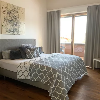A modern bedroom with a large bed and decorative pillows.
Large windows let in plenty of daylight and showcase an attractive wooden floor.