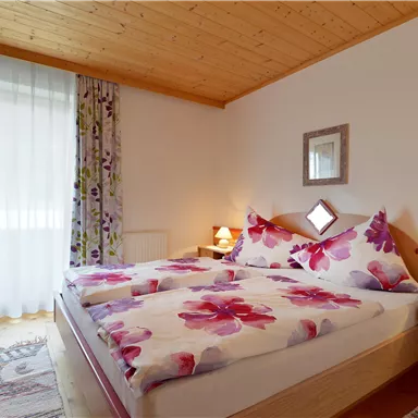 Ein gemütliches Schlafzimmer mit einem Doppelbett und bunten Blumenmustern. Die Raumgestaltung ist hell und einladend, mit sanftem Licht von den Tischlampen.
