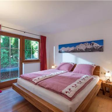 A cozy bedroom with two beds and comfortable bedding. A large window lets in natural light and offers a view of the greenery.