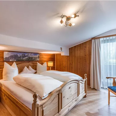 A cozy bedroom with a wooden bed and light pillows. Large French doors provide plenty of daylight and offer a beautiful view outside.