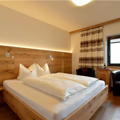 Ein modernes Schlafzimmer mit Holzwänden und zwei Betten. Ein gemütlicher Sessel und große Fenster sorgen für viel Licht.