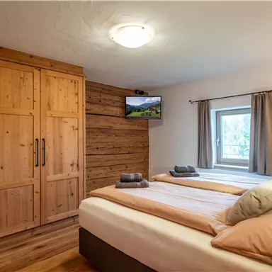 A cozy bedroom with two beds and wooden-paneled walls. There is a television and a window sill with a view from the window.