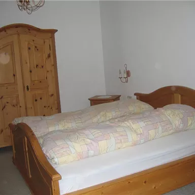 A simple bedroom with a large wooden bed and a chest of drawers. The walls are painted in neutral colors.