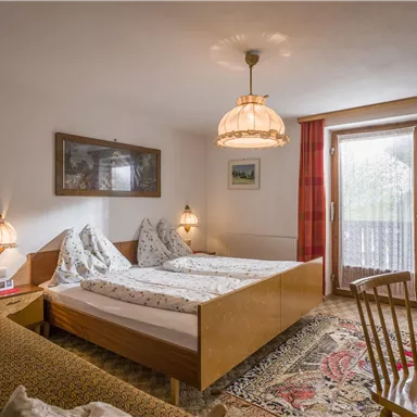 A cozy bedroom with two beds and a balcony. The decor is warm and inviting, with a nice rug and soft lighting.