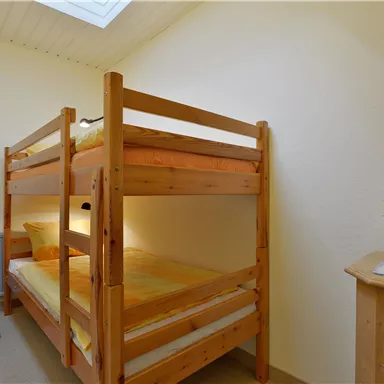 A simple room with a wooden loft bed and two mattresses. A chair and a small plant are also present.