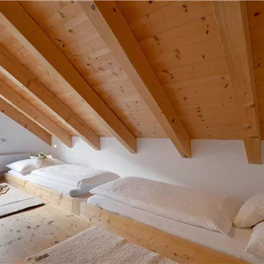 Eine gemütliche Dachgeschosszimmer mit Holzdecken und zwei Betten. Es gibt einen schönen Ausblick durch das Fenster und einige Dekokissen.