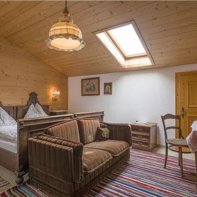 A cozy room with wooden paneling and two bed frames. A couch and a table complement the rustic furnishings.
