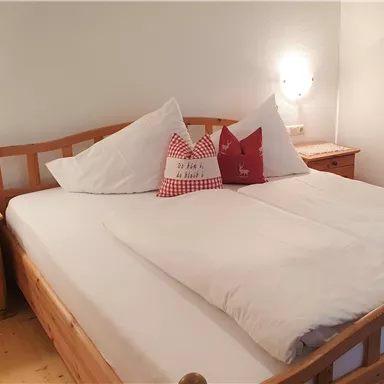 Ein gemütliches Schlafzimmer mit einem großen Doppelbett und hellen Kissen. Es gibt Holzmöbel und sanfte Beleuchtung.