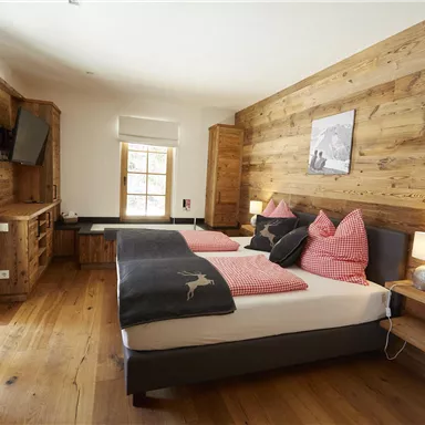 Ein gemütliches Schlafzimmer mit Holzwänden und zwei Betten. Die dekorativen Kissen in Rosa und Schwarz verleihen dem Raum eine einladende Atmosphäre.