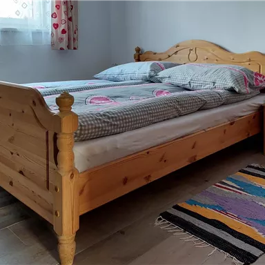 Ein gemütliches Schlafzimmer mit einem hölzernen Bett und bunten Bettwäsche. Neben dem Bett steht ein Nachttisch mit einer kleinen Lampe und einem Teppich auf dem Boden.