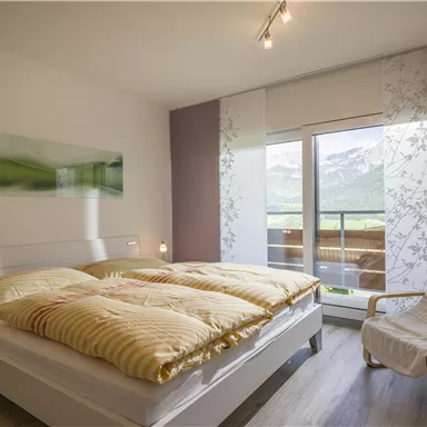 A cozy bedroom with a large bed and a beautiful view of the mountains. The room has bright colors and plenty of daylight.