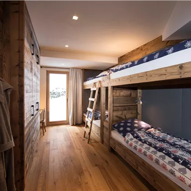 Ein gemütliches Zimmer mit einem Etagenbett und Holzverkleidung. Große Fenster bieten einen Blick ins Freie und viel Tageslicht.