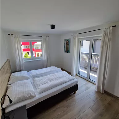 A bright bedroom with a double bed and modern furniture. Large windows provide plenty of daylight and access to the balcony.