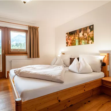 Ein gemütliches Schlafzimmer mit einem großen Bett und zwei Kissen. Die Fenster bieten einen Blick auf die Berge und lassen viel Licht hinein.