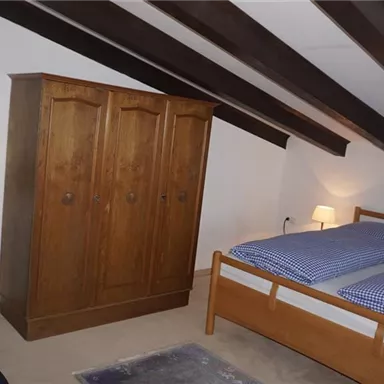 Ein gemütliches Schlafzimmer mit einem Doppelbett und einer Holzkiste. Die Wände sind mit Bildern dekoriert und es gibt eine Stehlampe in der Ecke.