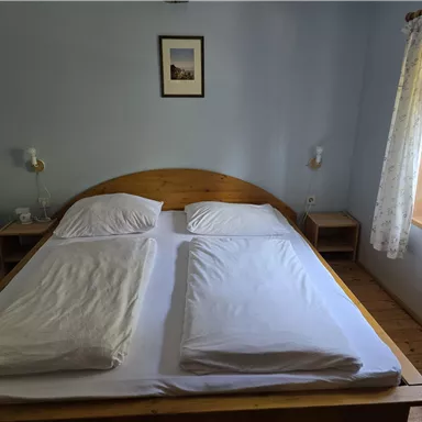 Ein gemütliches Schlafzimmer mit einem Doppelbett und einfachen Holzmöbeln. Das Fenster lässt viel Tageslicht herein und es gibt einen schönen Blick nach draußen.