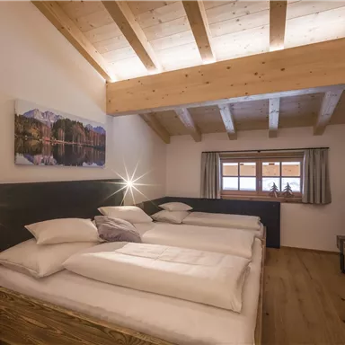 A cozy bedroom with a wooden ceiling and three beds. Large windows provide plenty of daylight and a view outside.