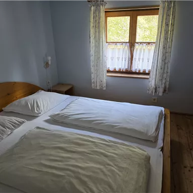 Ein einfaches Schlafzimmer mit einem Doppelbett und zwei Kissen. Das Zimmer hat einen Fenster mit Vorhängen und Holzboden.