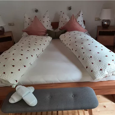 Ein gemütliches Schlafzimmer mit einem großen Bett und dekorativen Kissen. Neben dem Bett befinden sich Nachttische mit Lampen.