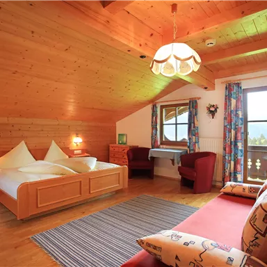 Ein gemütliches Dachzimmer mit Holzwänden und einem großen Bett. Es gibt eine Sitzecke und einen schönen Ausblick durch das Fenster.