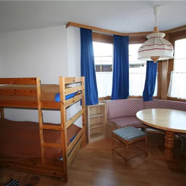 A cozy room with a bunk bed and a round table. Bright windows with blue curtains create a friendly atmosphere.