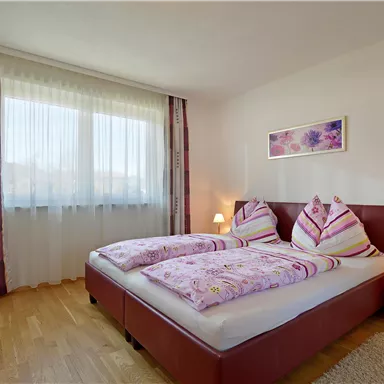 Ein gemütliches Schlafzimmer mit zwei Betten und bunten Bettwäsche. Große Fenster sorgen für viel Tageslicht.