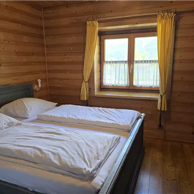 Ein gemütliches Schlafzimmer mit zwei Betten und Holzverkleidung. Die Fenster sind mit gelben Vorhängen versehen und bieten Tageslicht.