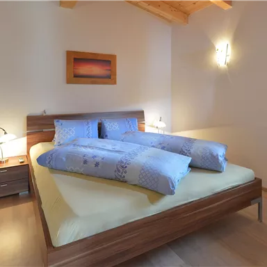 Ein gemütliches Schlafzimmer mit einem großen Bett und Holzdecke. Das Zimmer ist hell und freundlich, mit sanften Farben und einem Fenster.