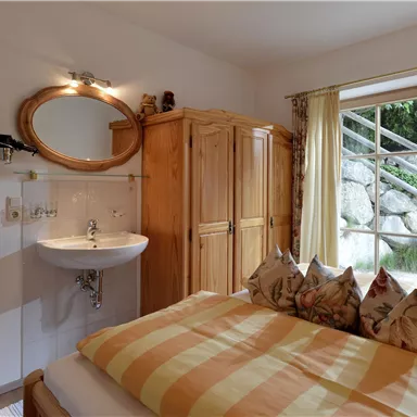 A cozy bedroom with two beds and a wooden wardrobe. Large windows provide plenty of natural light and a view of nature.