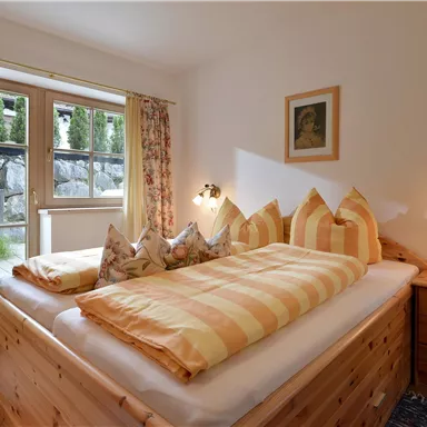 A bright bedroom with a large bed and colorful pillows. The windows offer a view of the outside landscape.
