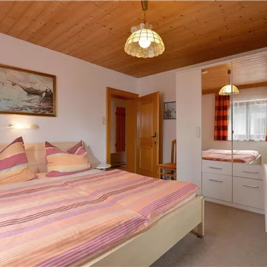 Ein gemütliches Schlafzimmer mit einem Doppelbett und bunten Kissen. Im Hintergrund sind ein Spiegel und ein Holzdecken zu sehen.