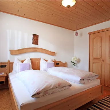 Ein gemütliches Schlafzimmer mit einem großen Doppelbett und Holzdekor. Der Raum ist hell und einladend, mit einem Schrank und einem Teppich.