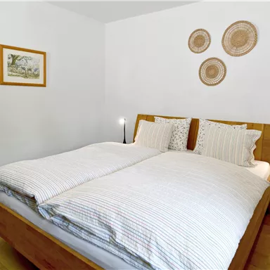 Ein modernes Schlafzimmer mit einem Doppelbett und gestreiften Bettdecken. An der Wand hängen dekorative Wandobjekte und ein kleines Bild.