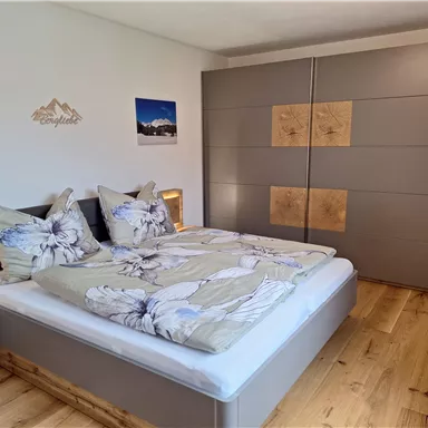 Ein gemütliches Schlafzimmer mit einem großen Bett und schönen Blumenmustern auf der Bettwäsche. Der Raum hat Holzfußboden und einen modernen Kleiderschrank.