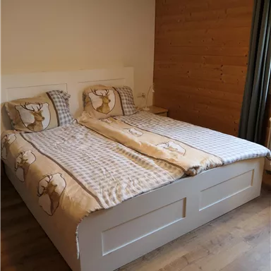 Ein gemütliches Schlafzimmer mit einem Doppelbett und Holzverkleidung. Die Bettwäsche ist in sanften Farben mit einem Tiermotiv.